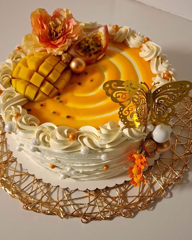 Gâteau mangue passion nappé de coulis, orné de crème, de mangue et d'un papillon doré